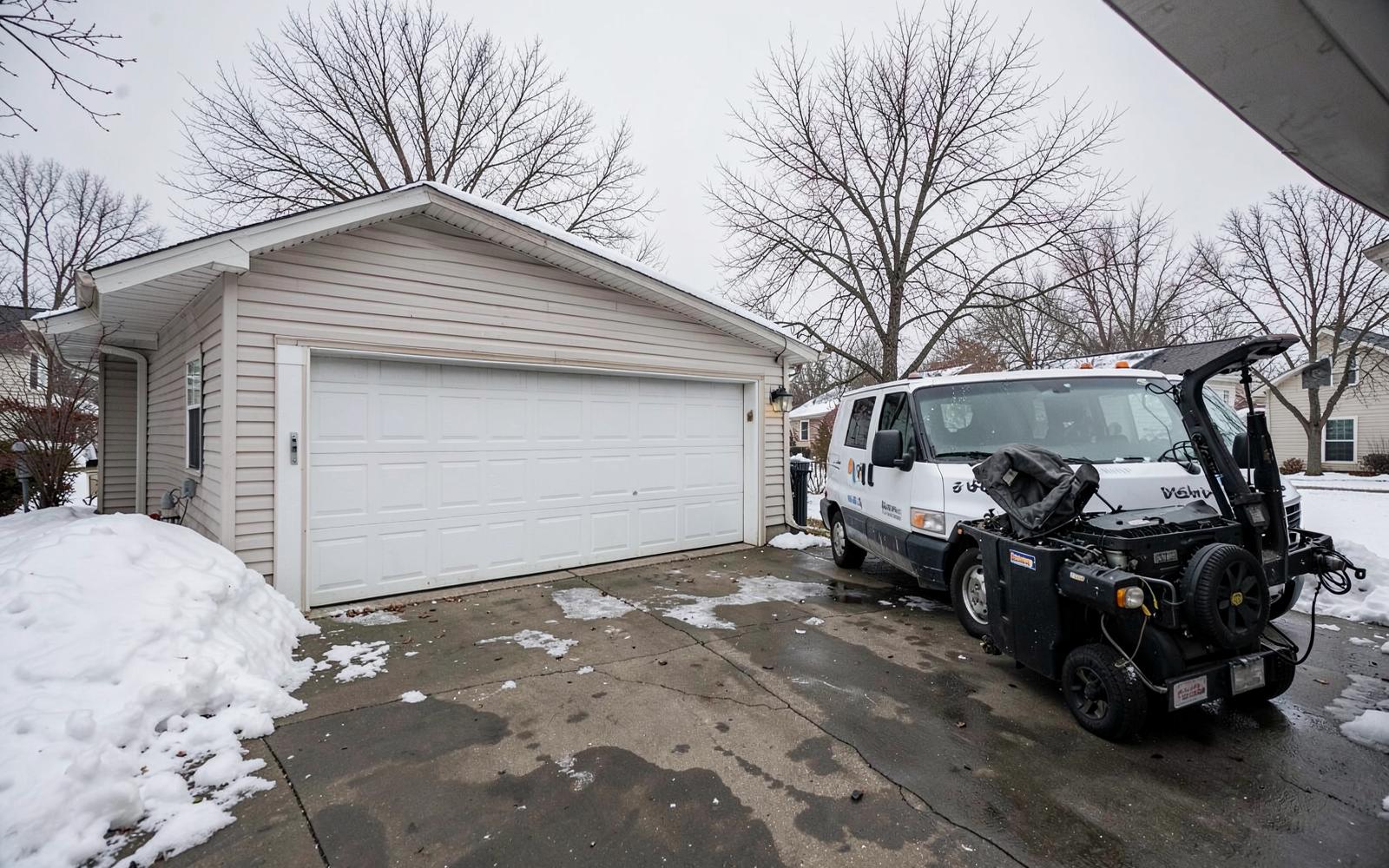Snowy Wisconsin driveway with a two-car garage door and a service van parked outside
